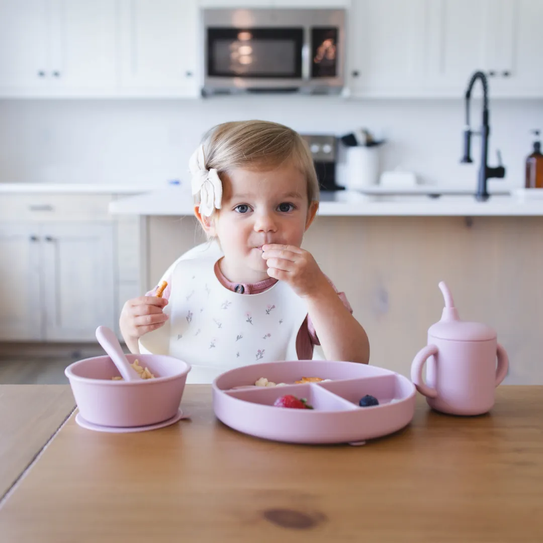 A toddler eating at a kitchen table wearing the ivory KAYA bib with a wildflower print