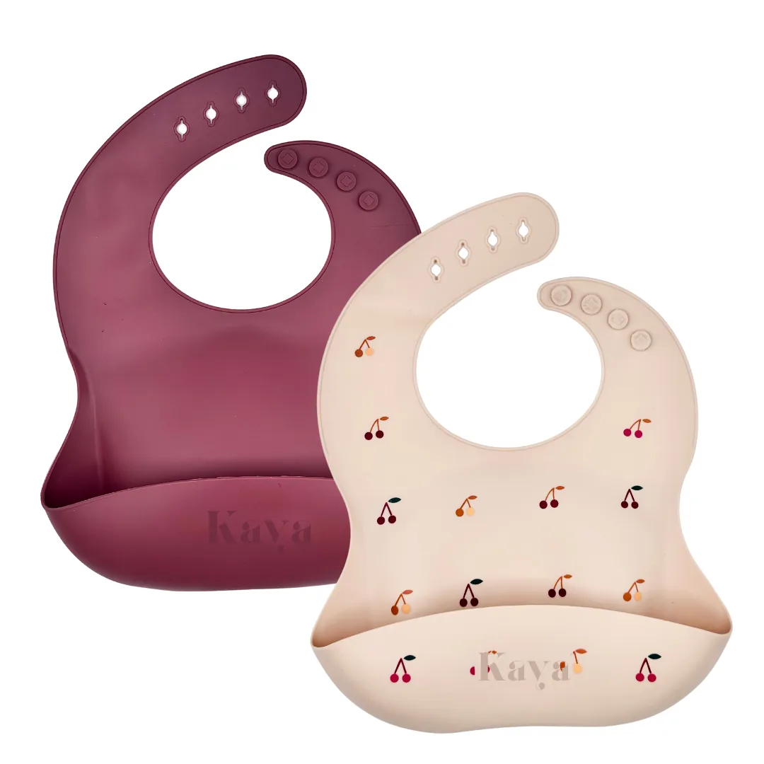 KAYA 2-pack of silicone baby bibs: a deep mauve bib and a cream bib with a cherry print, each with a food-catcher pocket