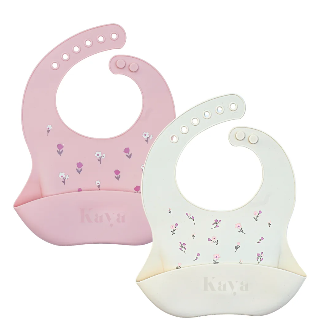 KAYA 2-pack of silicone baby bibs in pink and ivory white, both with a small wildflower print and a deep food-catcher pocket